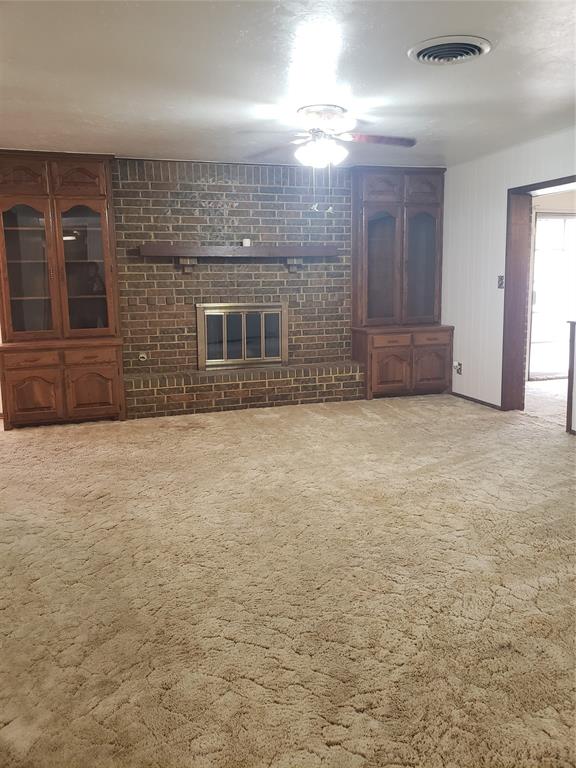 unfurnished living room featuring carpet flooring, ceiling fan, brick wall, and a brick fireplace