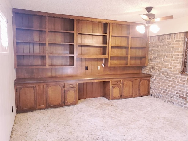 unfurnished office with ceiling fan, brick wall, a textured ceiling, light carpet, and built in desk