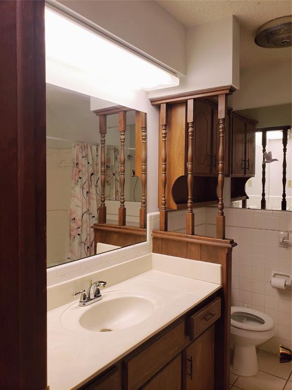 bathroom featuring walk in shower, tile patterned flooring, toilet, vanity, and tile walls