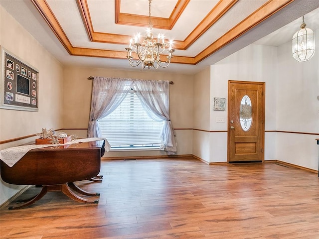 foyer with wood-type flooring, a tray ceiling, an inviting chandelier, and ornamental molding