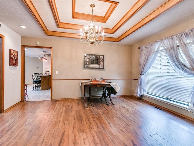 dining room with a notable chandelier, light hardwood / wood-style floors, a raised ceiling, and a textured ceiling