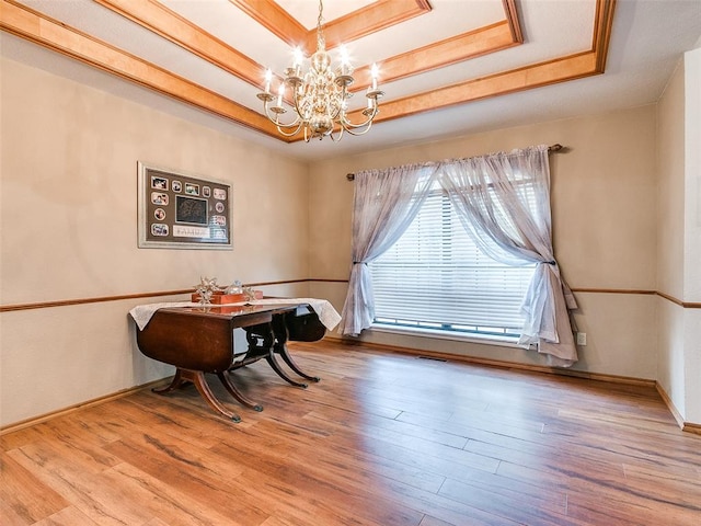 dining area with a raised ceiling, wood-type flooring, and a chandelier