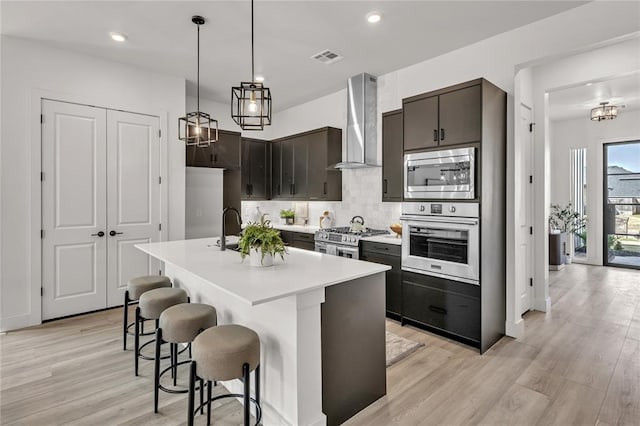 kitchen featuring pendant lighting, wall chimney exhaust hood, decorative backsplash, light hardwood / wood-style floors, and stainless steel appliances