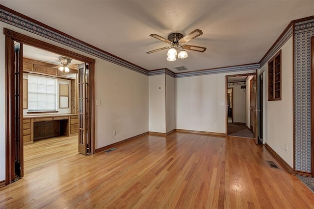 spare room with ceiling fan, built in desk, light wood-type flooring, and ornamental molding