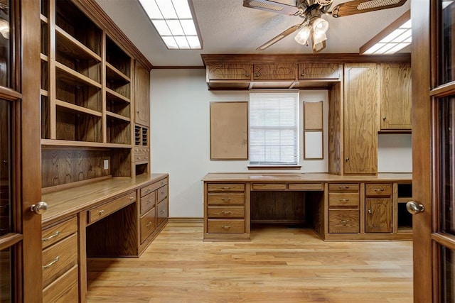 office space with ceiling fan, built in desk, ornamental molding, and light hardwood / wood-style flooring