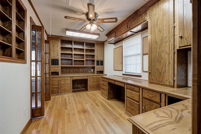 unfurnished office featuring french doors, built in desk, light hardwood / wood-style floors, and ceiling fan