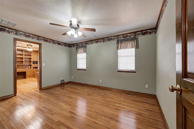 spare room with built in shelves, built in desk, light wood-type flooring, and a textured ceiling