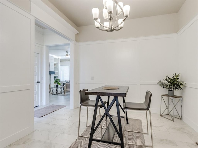 dining space with marble finish floor, a decorative wall, and ceiling fan with notable chandelier