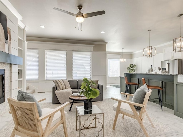 living area with recessed lighting, crown molding, a tiled fireplace, and ceiling fan with notable chandelier