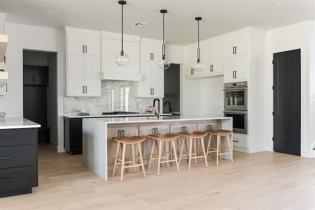 kitchen with white cabinets, appliances with stainless steel finishes, light wood-type flooring, and a kitchen island with sink