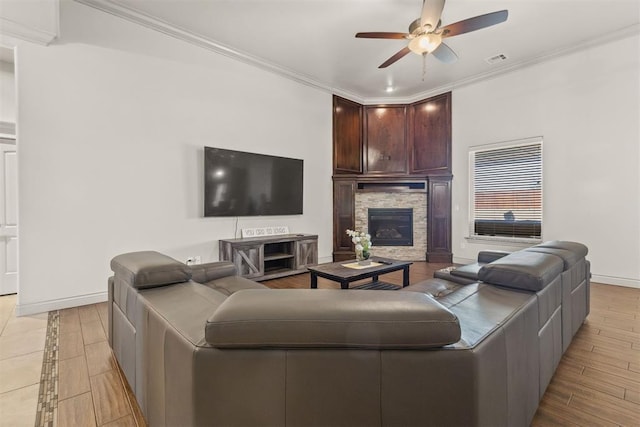 living room featuring ceiling fan, a stone fireplace, light wood-type flooring, and ornamental molding