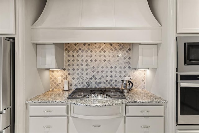 kitchen featuring backsplash, white cabinetry, light stone countertops, and appliances with stainless steel finishes