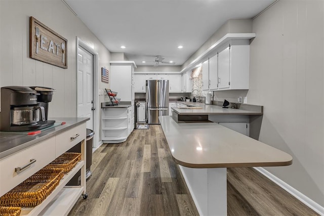 kitchen featuring wood-type flooring, sink, a kitchen bar, white cabinetry, and stainless steel refrigerator