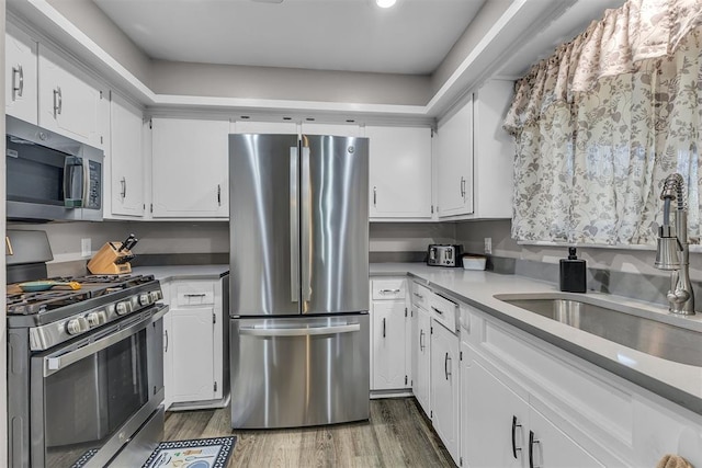 kitchen with appliances with stainless steel finishes, dark hardwood / wood-style floors, white cabinetry, and sink