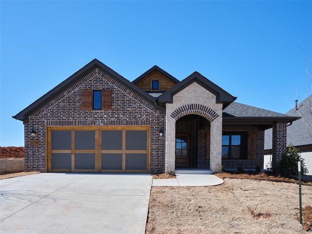 view of front of property featuring an attached garage, brick siding, driveway, stone siding, and roof with shingles