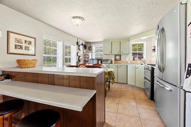 kitchen featuring a kitchen breakfast bar, green cabinetry, a textured ceiling, kitchen peninsula, and stainless steel appliances