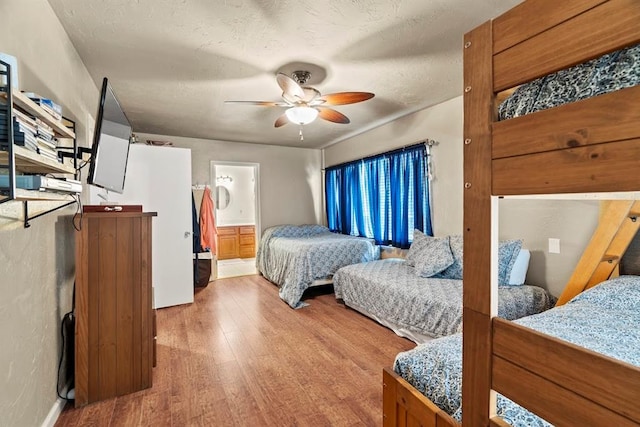 bedroom with ceiling fan, wood-type flooring, a textured ceiling, and ensuite bath