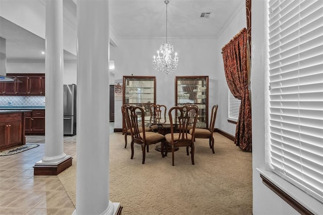 carpeted dining area featuring ornate columns, crown molding, and an inviting chandelier