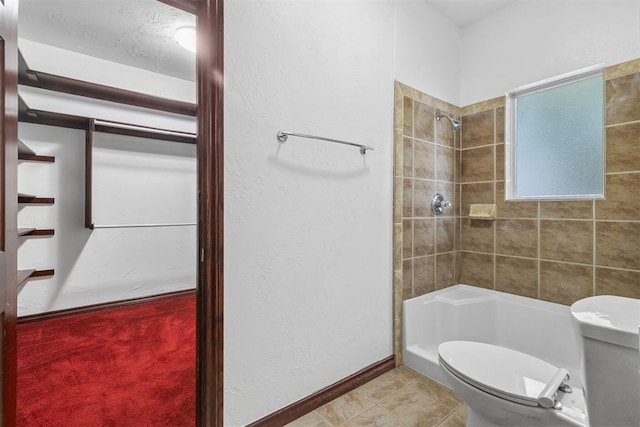 bathroom with toilet, a tile shower, and tile patterned floors