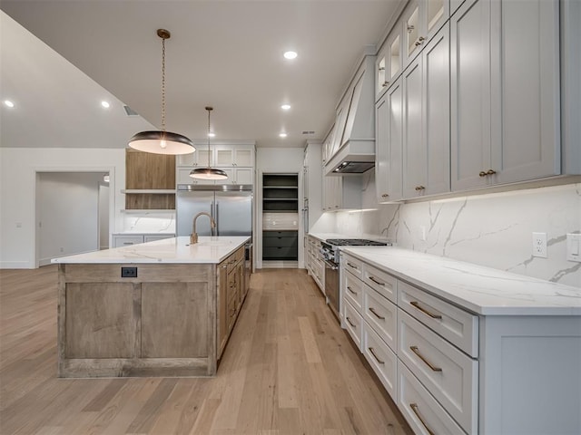 kitchen with light stone counters, high end appliances, hanging light fixtures, and a large island with sink