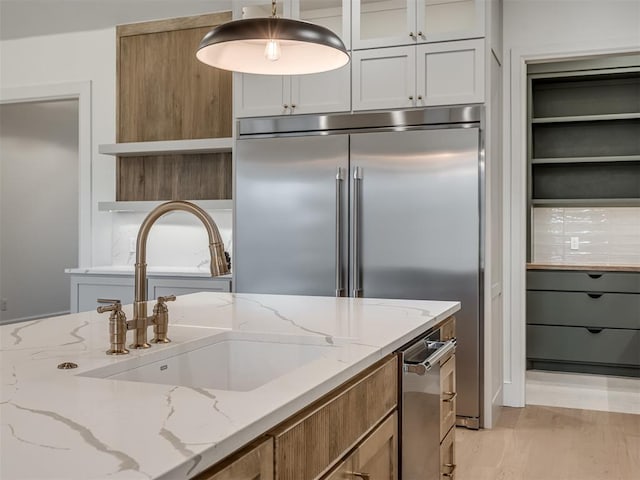 kitchen with light stone countertops, sink, decorative light fixtures, light hardwood / wood-style flooring, and white cabinetry