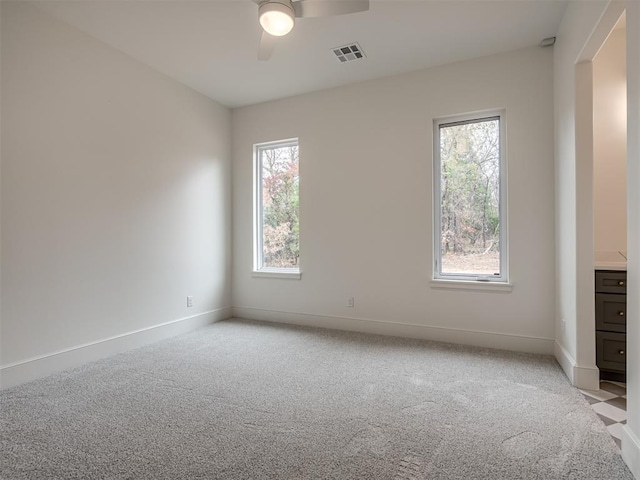 spare room featuring ceiling fan, light colored carpet, and a healthy amount of sunlight