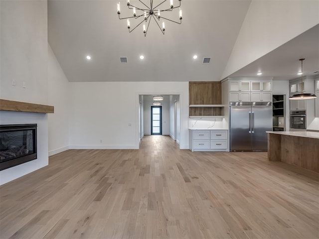 kitchen with hanging light fixtures, high vaulted ceiling, light hardwood / wood-style floors, white cabinets, and appliances with stainless steel finishes