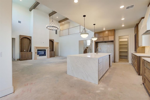 kitchen with white cabinetry, an island with sink, hanging light fixtures, a high ceiling, and a notable chandelier