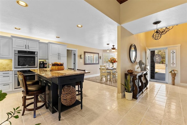 kitchen with gray cabinets, light stone countertops, double oven, a kitchen island, and a kitchen bar