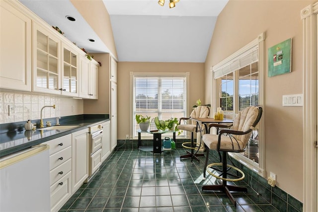 kitchen featuring white cabinetry, dishwasher, sink, tasteful backsplash, and lofted ceiling