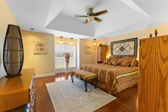 bedroom with a tray ceiling, ceiling fan, and dark wood-type flooring