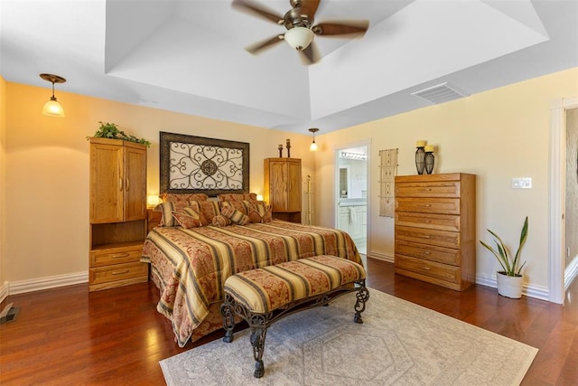 bedroom with ensuite bathroom, ceiling fan, dark hardwood / wood-style flooring, and a tray ceiling