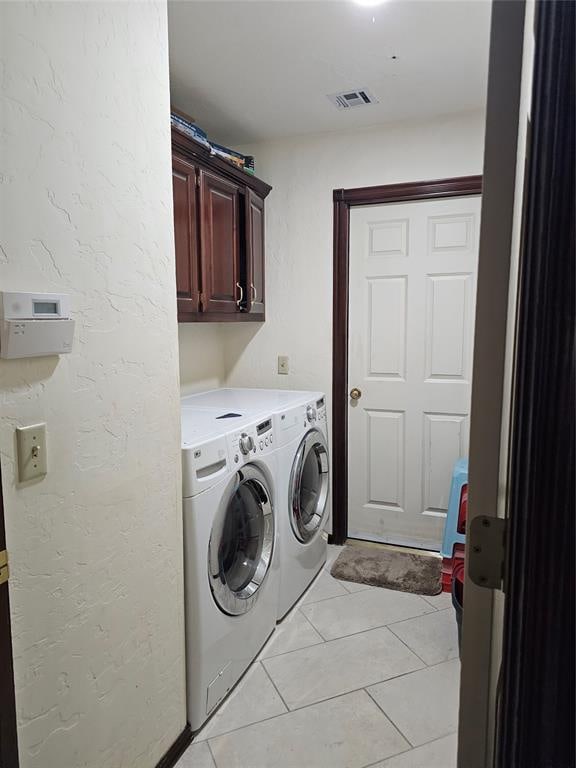 clothes washing area featuring cabinets, light tile patterned floors, and washing machine and dryer