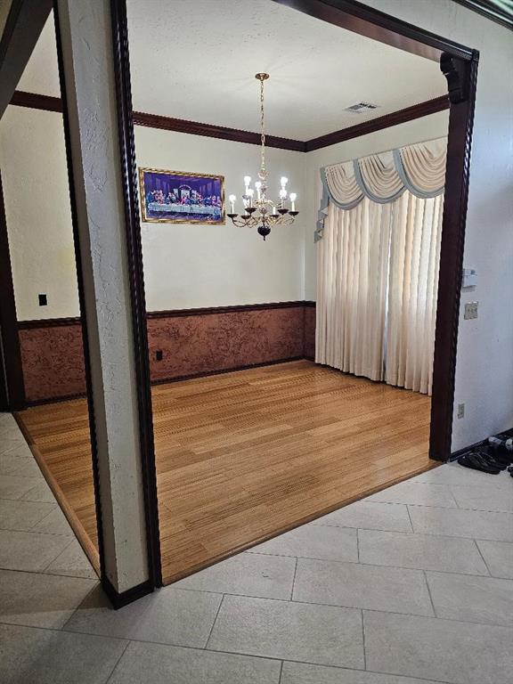 unfurnished dining area featuring wood-type flooring, crown molding, and an inviting chandelier