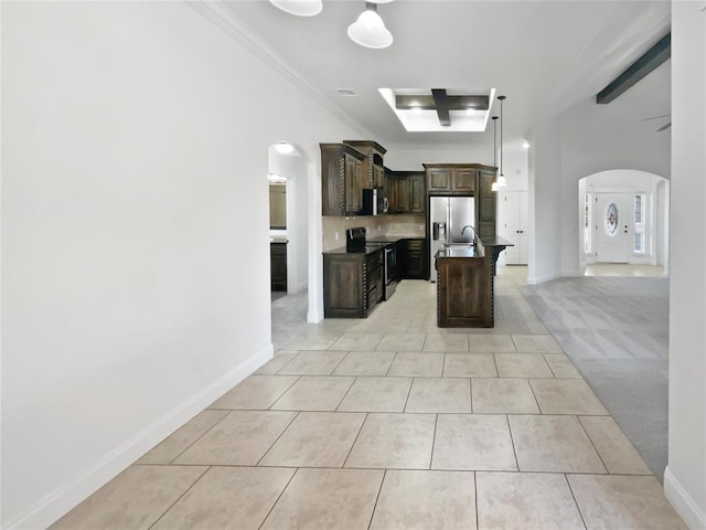 kitchen featuring appliances with stainless steel finishes, dark brown cabinets, light colored carpet, crown molding, and an island with sink