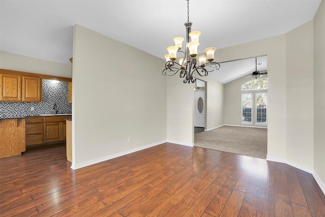 unfurnished dining area with stacked washing maching and dryer, ceiling fan with notable chandelier, sink, dark hardwood / wood-style floors, and lofted ceiling