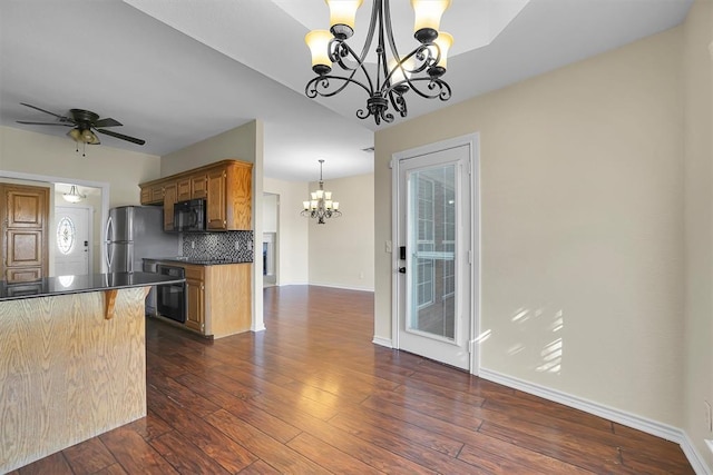 kitchen featuring ceiling fan with notable chandelier, dark hardwood / wood-style floors, decorative backsplash, a kitchen bar, and stainless steel refrigerator