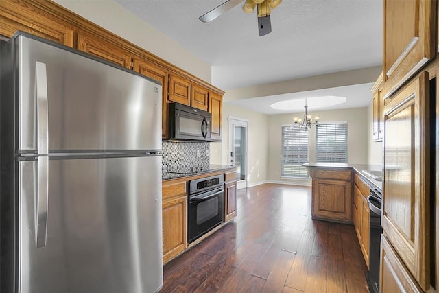 kitchen featuring dark wood-type flooring, tasteful backsplash, pendant lighting, black appliances, and ceiling fan with notable chandelier