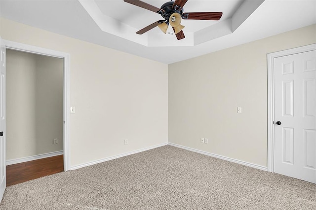 carpeted empty room featuring a raised ceiling and ceiling fan