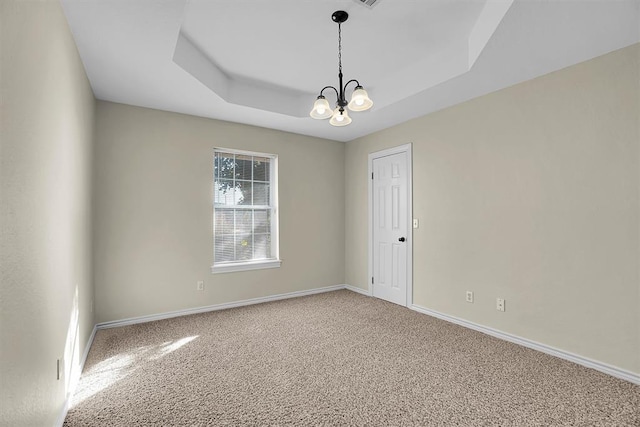 spare room featuring a raised ceiling, carpet floors, and a notable chandelier