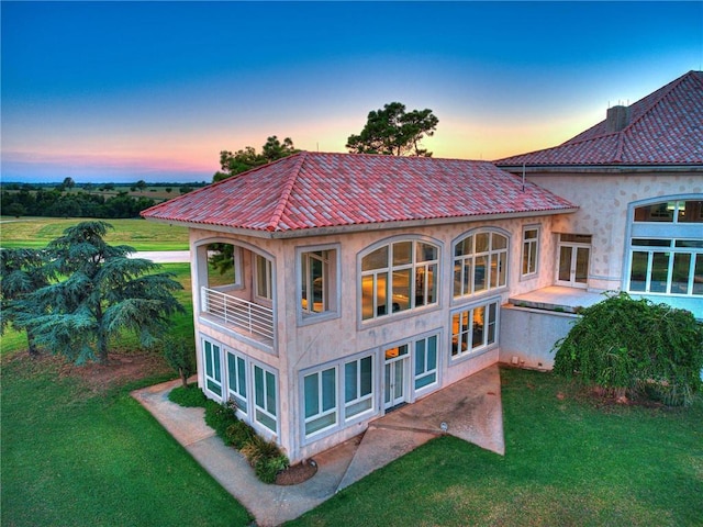 back house at dusk featuring a balcony, a yard, and french doors