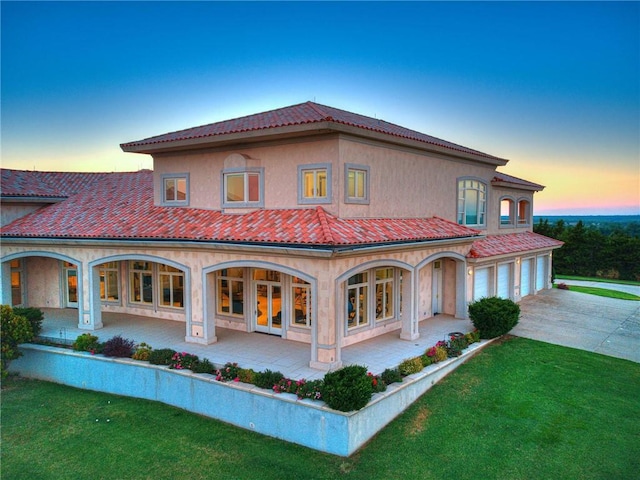 back house at dusk featuring a lawn, a porch, and a garage