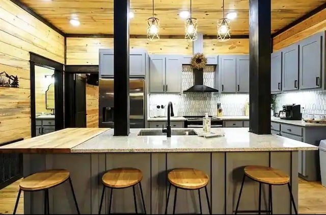 kitchen with a kitchen bar, a kitchen island with sink, wooden walls, sink, and decorative light fixtures