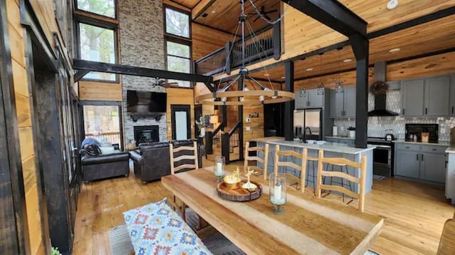 dining room featuring a stone fireplace, wooden ceiling, a towering ceiling, and light hardwood / wood-style flooring