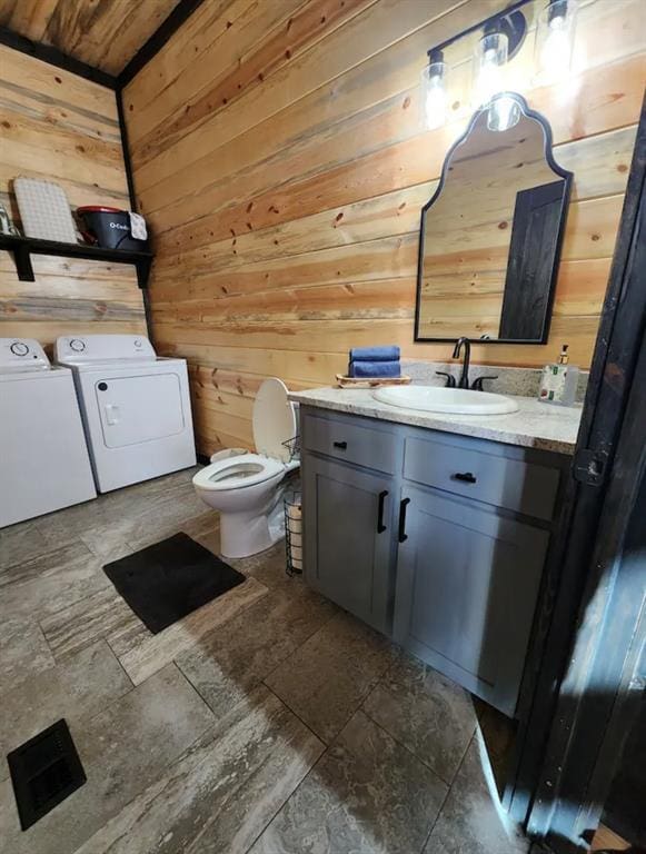 bathroom featuring washing machine and clothes dryer, wood walls, vanity, and toilet