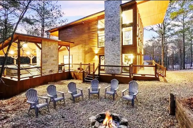 back house at dusk featuring a wooden deck and a fire pit