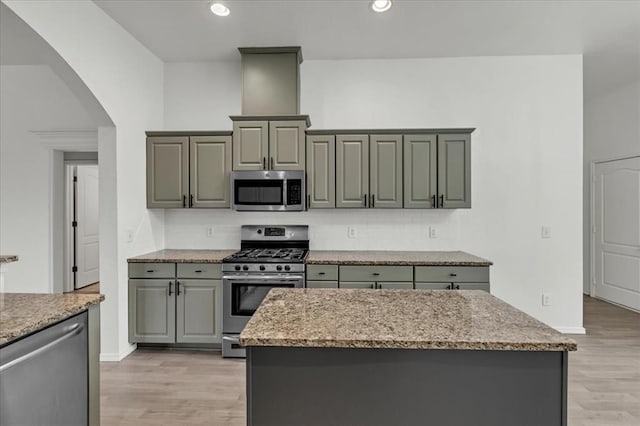 kitchen featuring a kitchen island, stainless steel appliances, light hardwood / wood-style floors, gray cabinets, and light stone counters