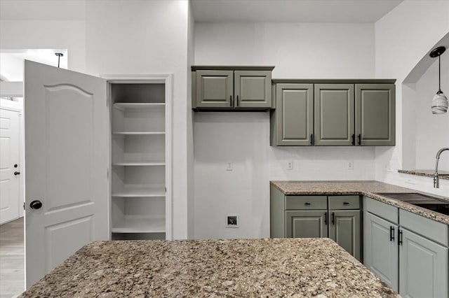 kitchen with light stone countertops, pendant lighting, hardwood / wood-style floors, sink, and gray cabinets