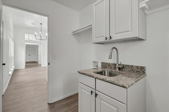 kitchen featuring white cabinetry, light hardwood / wood-style floors, sink, a notable chandelier, and light stone counters