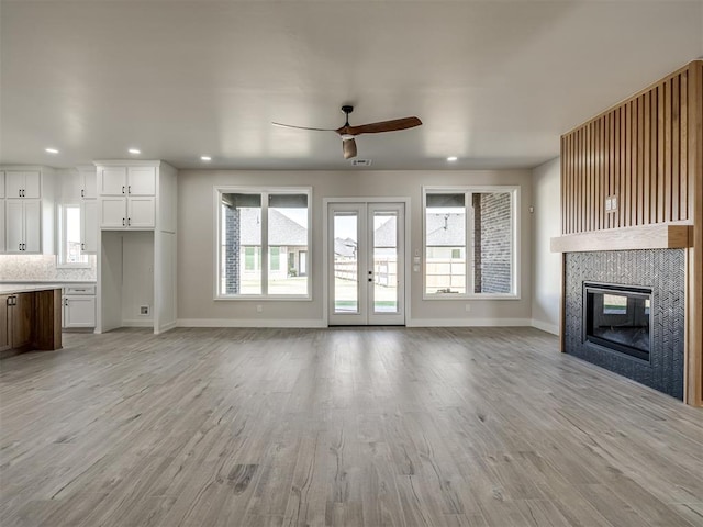 unfurnished living room featuring ceiling fan, light hardwood / wood-style floors, a fireplace, and french doors